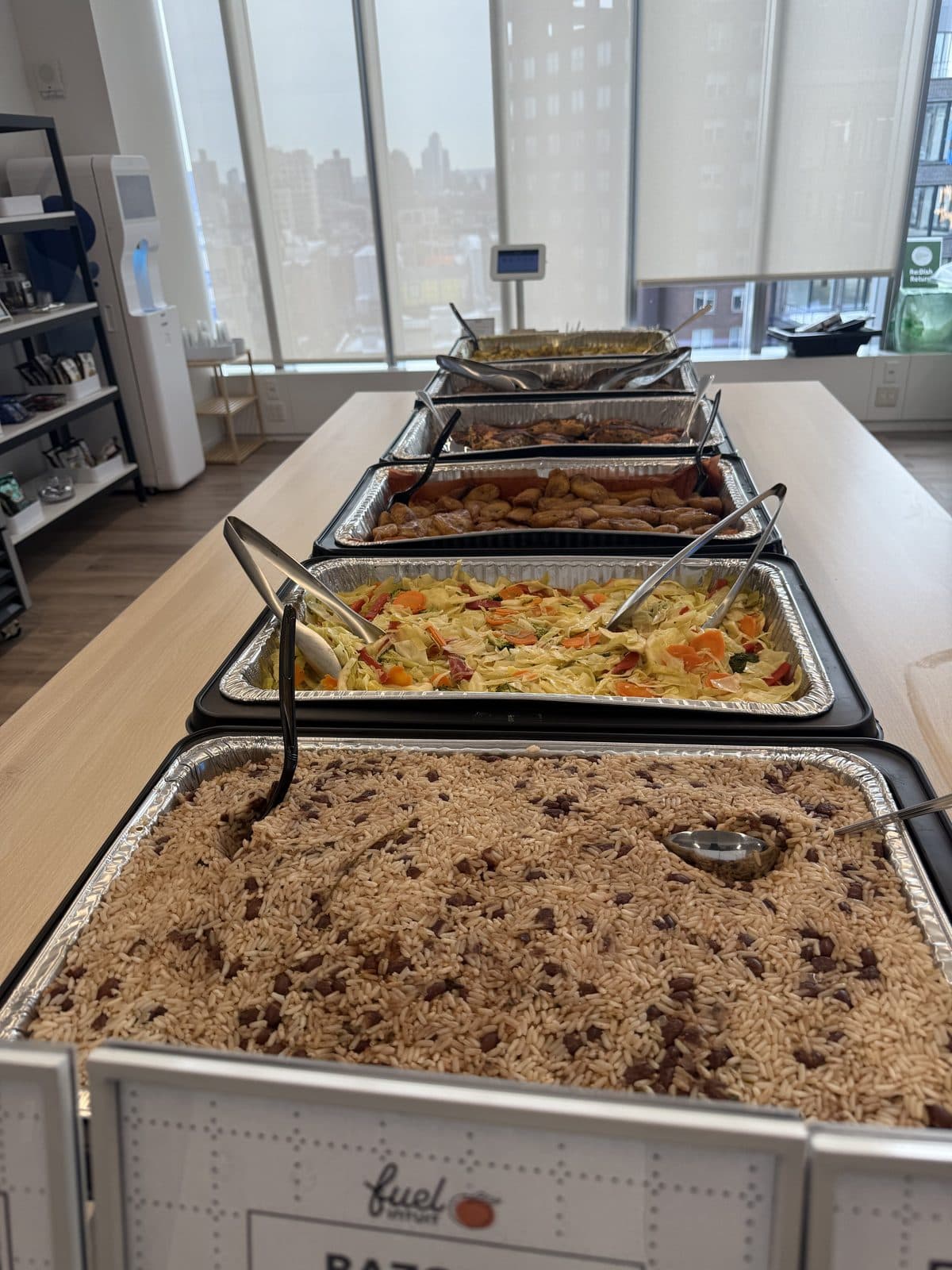 Catering trays of rice and peas, cabbage slaw, plantain, and chicken set up buffet-style