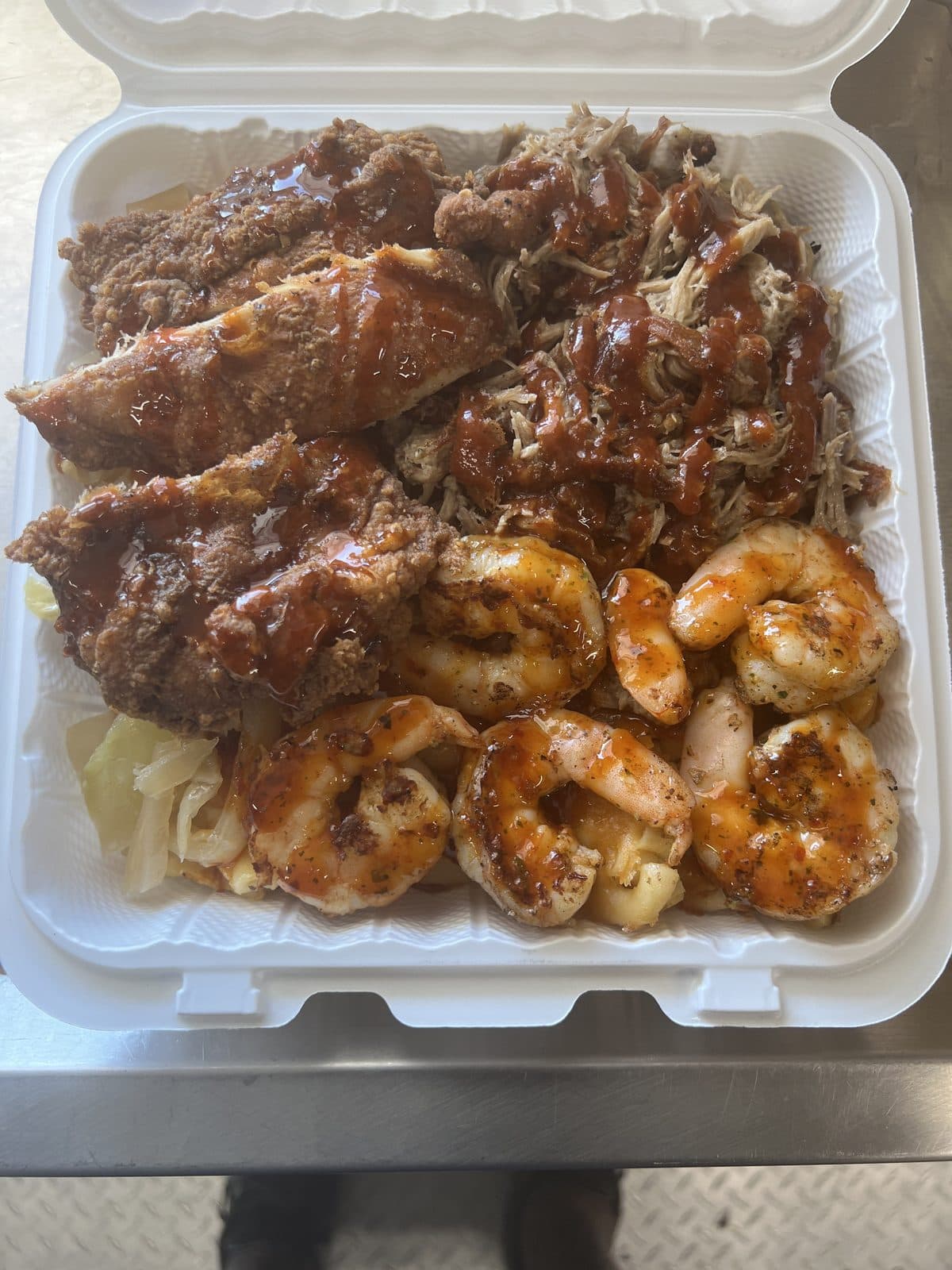 A boxed plate of BBQ pulled meat, fried chicken, and seasoned shrimp